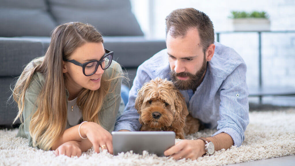 Young couple with dog on floor looking at tablet